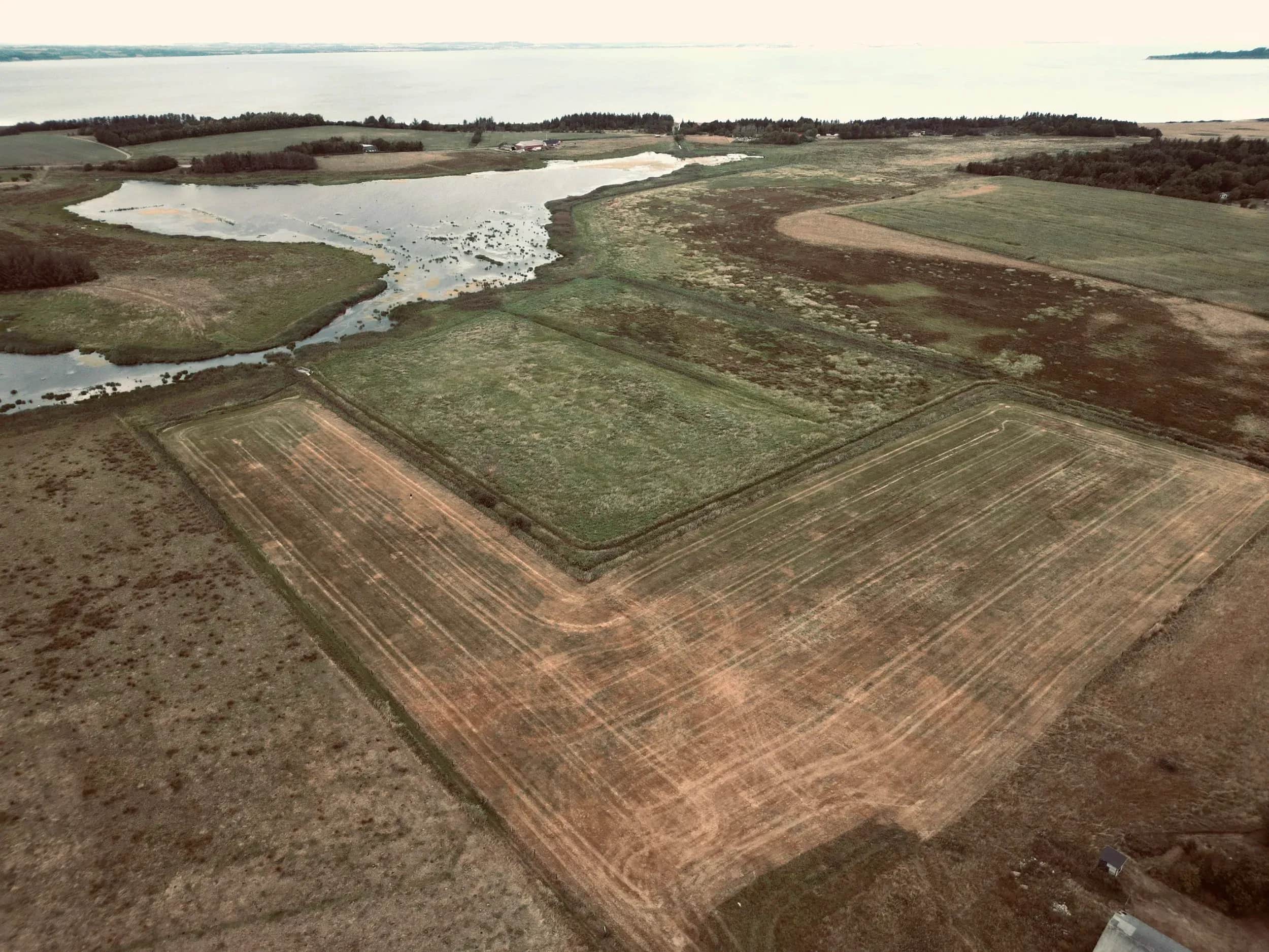 Luchtfoto van velden en een fjordarm met eilanden aan de horizon.