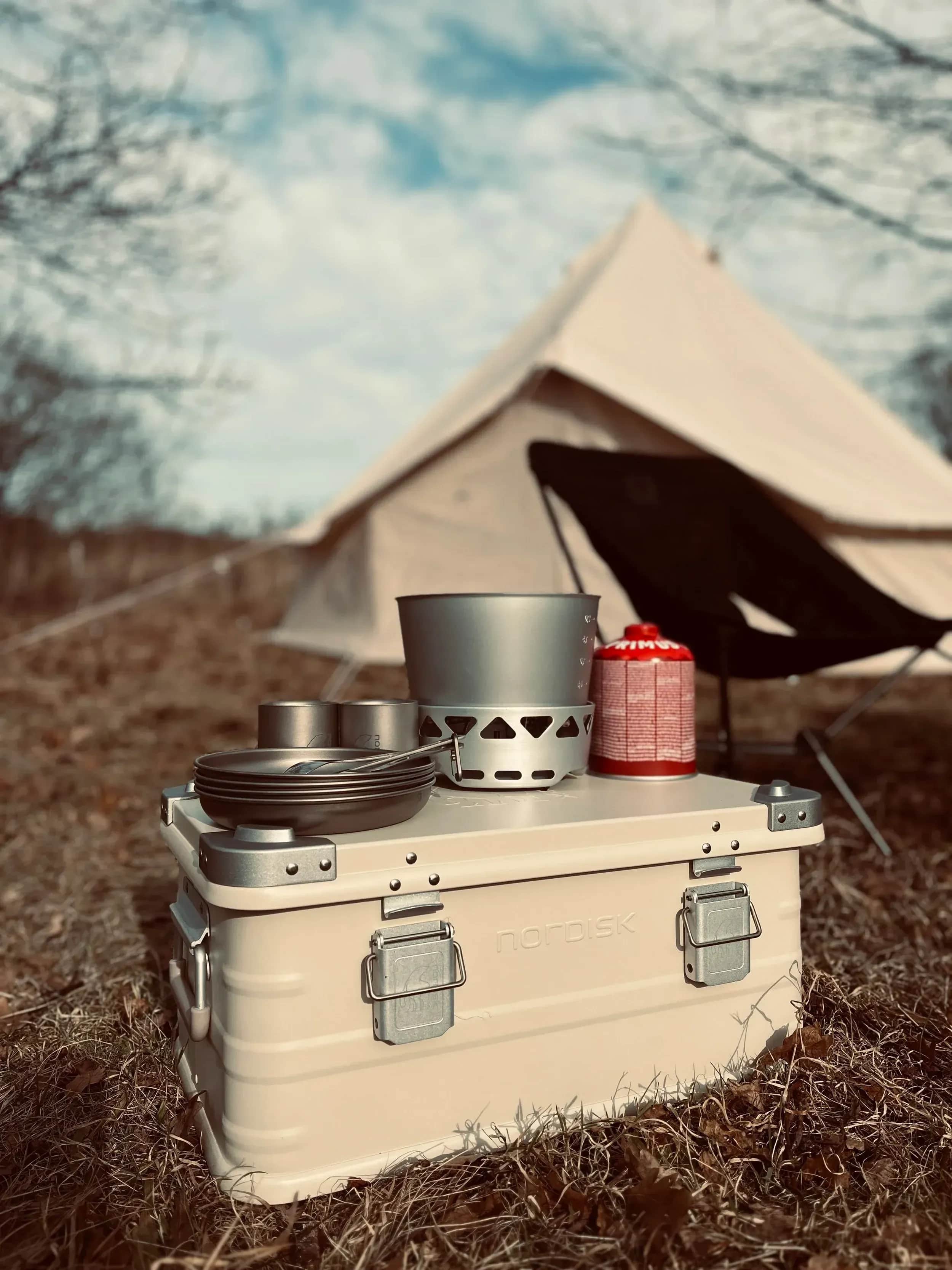 Beige telt, campingstol og en køleboks med kogegrej.