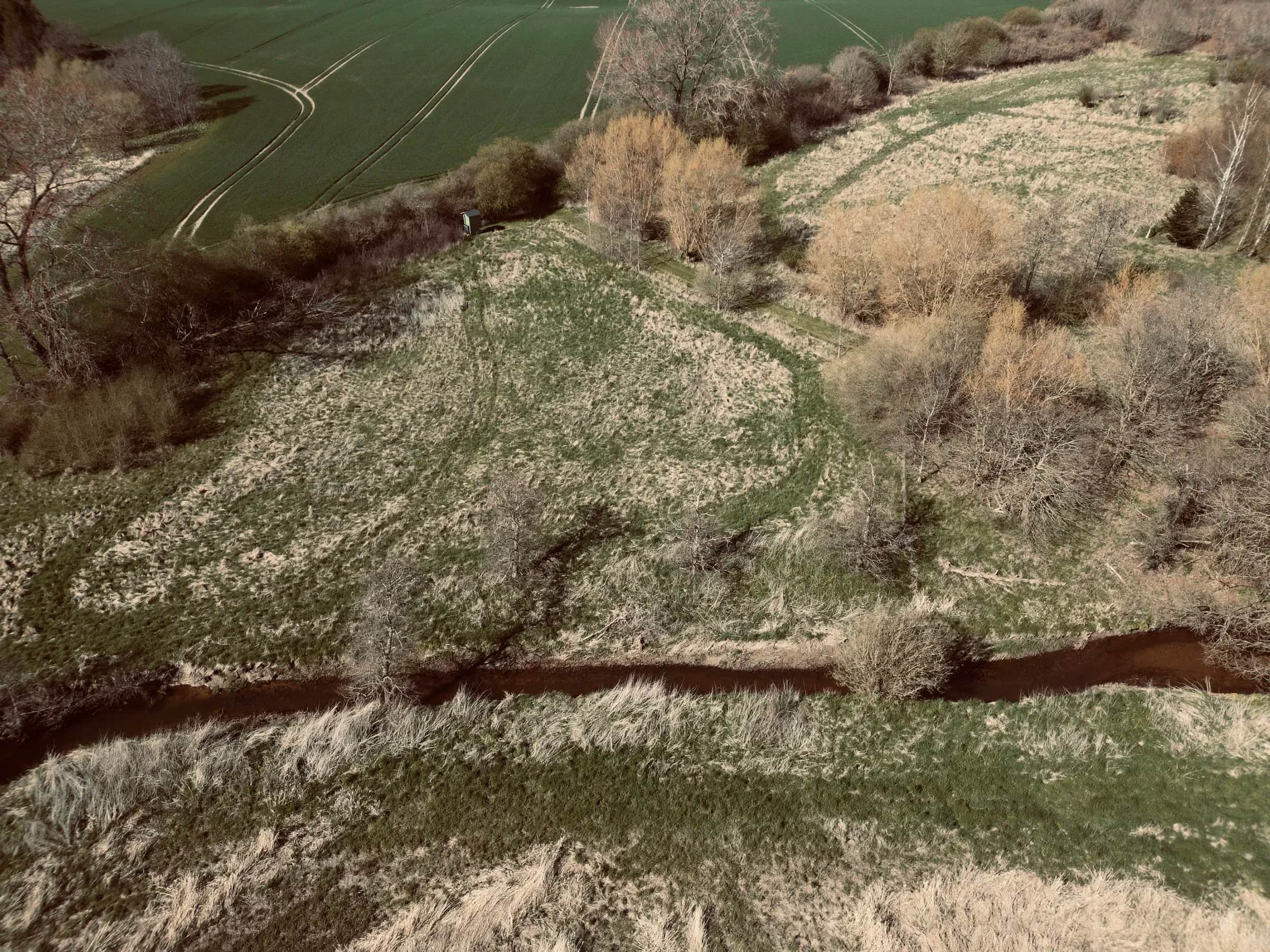 Luchtfoto van een beek door velden en kale bomen.
