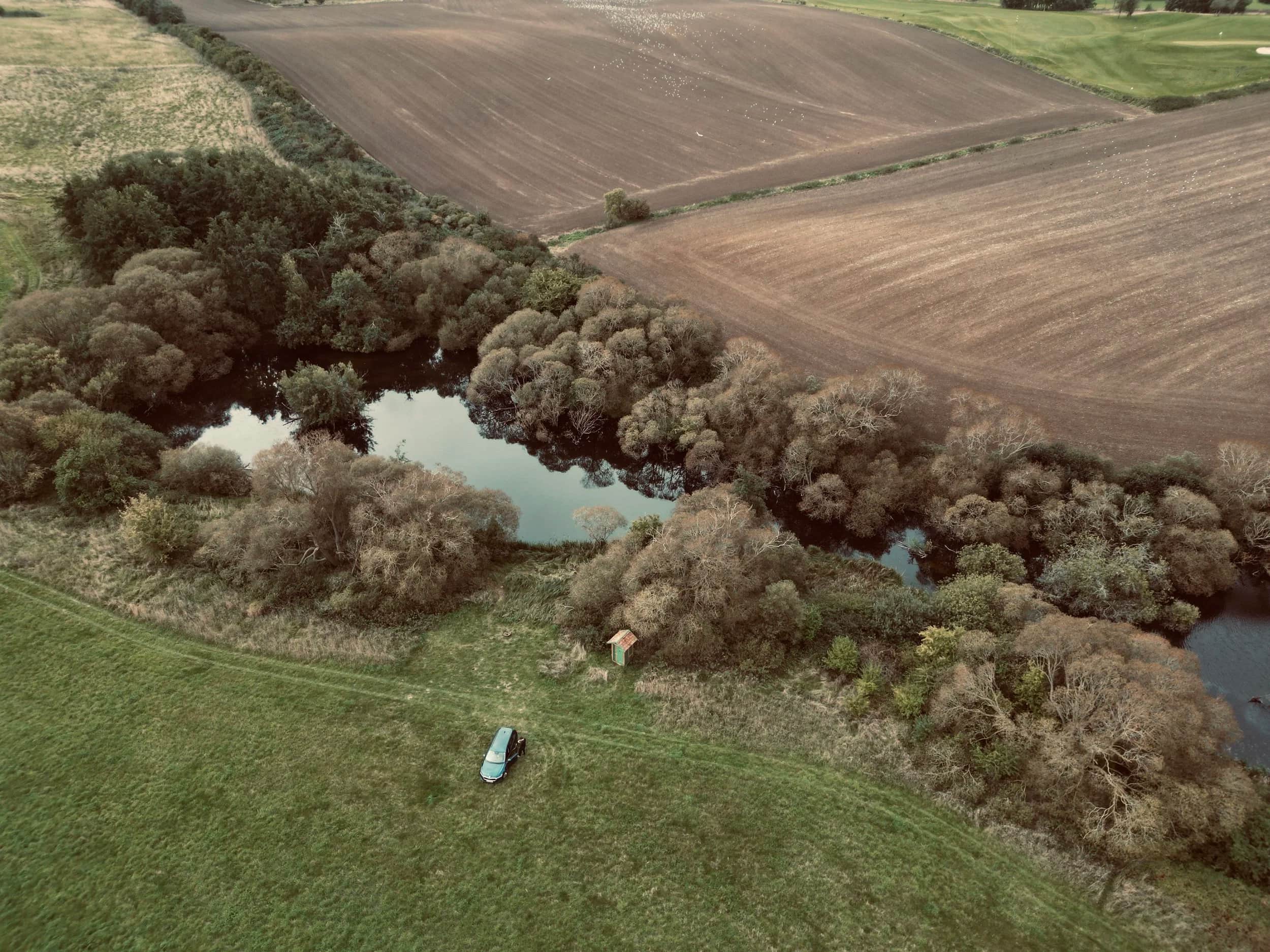 Luchtfoto van een meer omringd door bomen, met een tent op de weide.