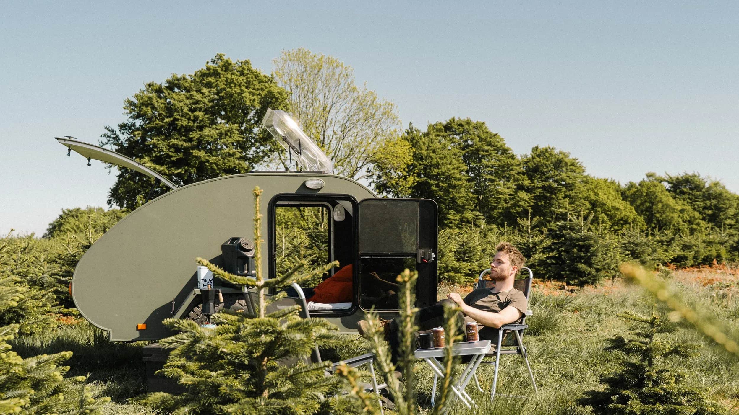 Person sidder i en stol ved en åben campingvogn set oppefra.