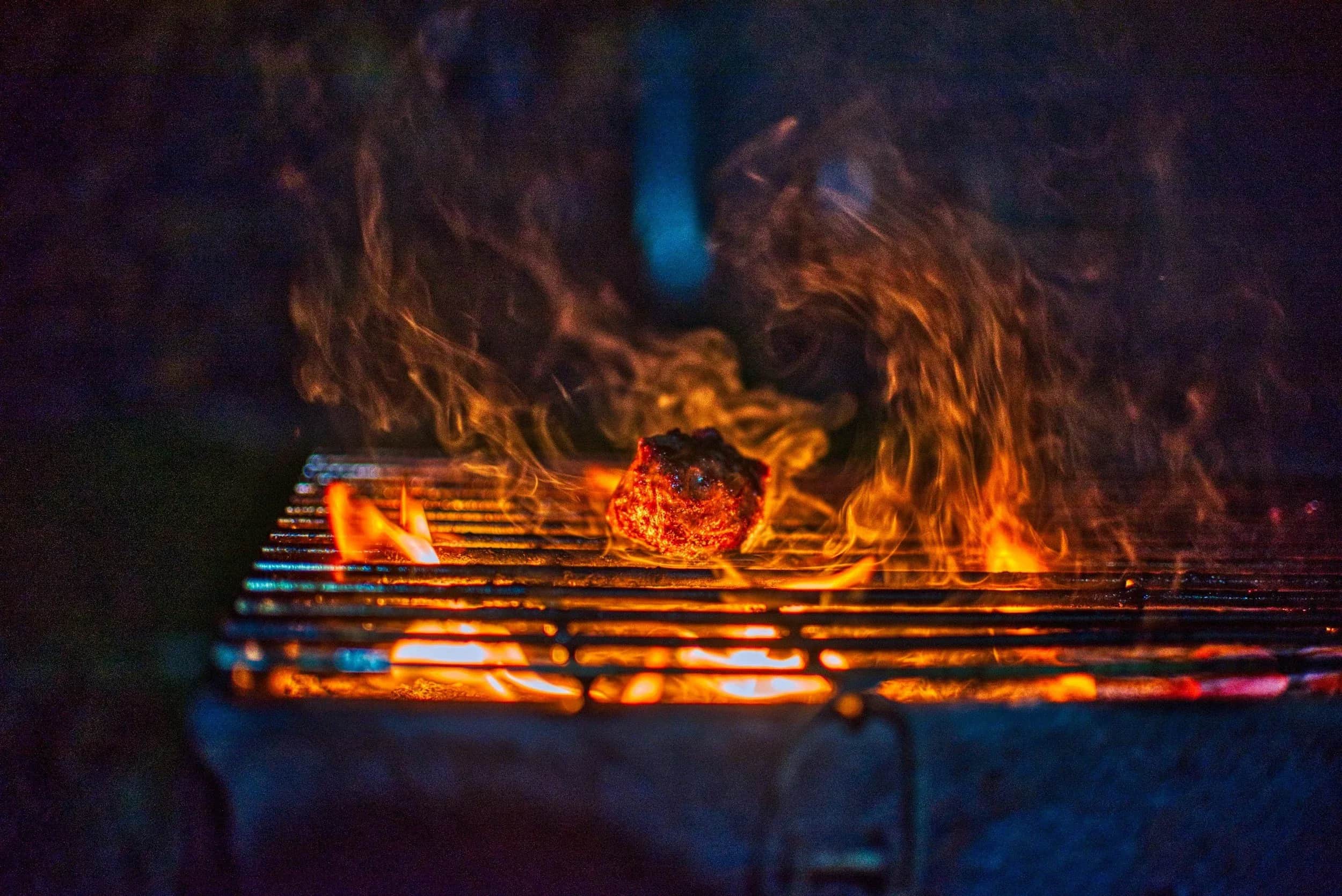 Flammer under en grillrist over et bål.