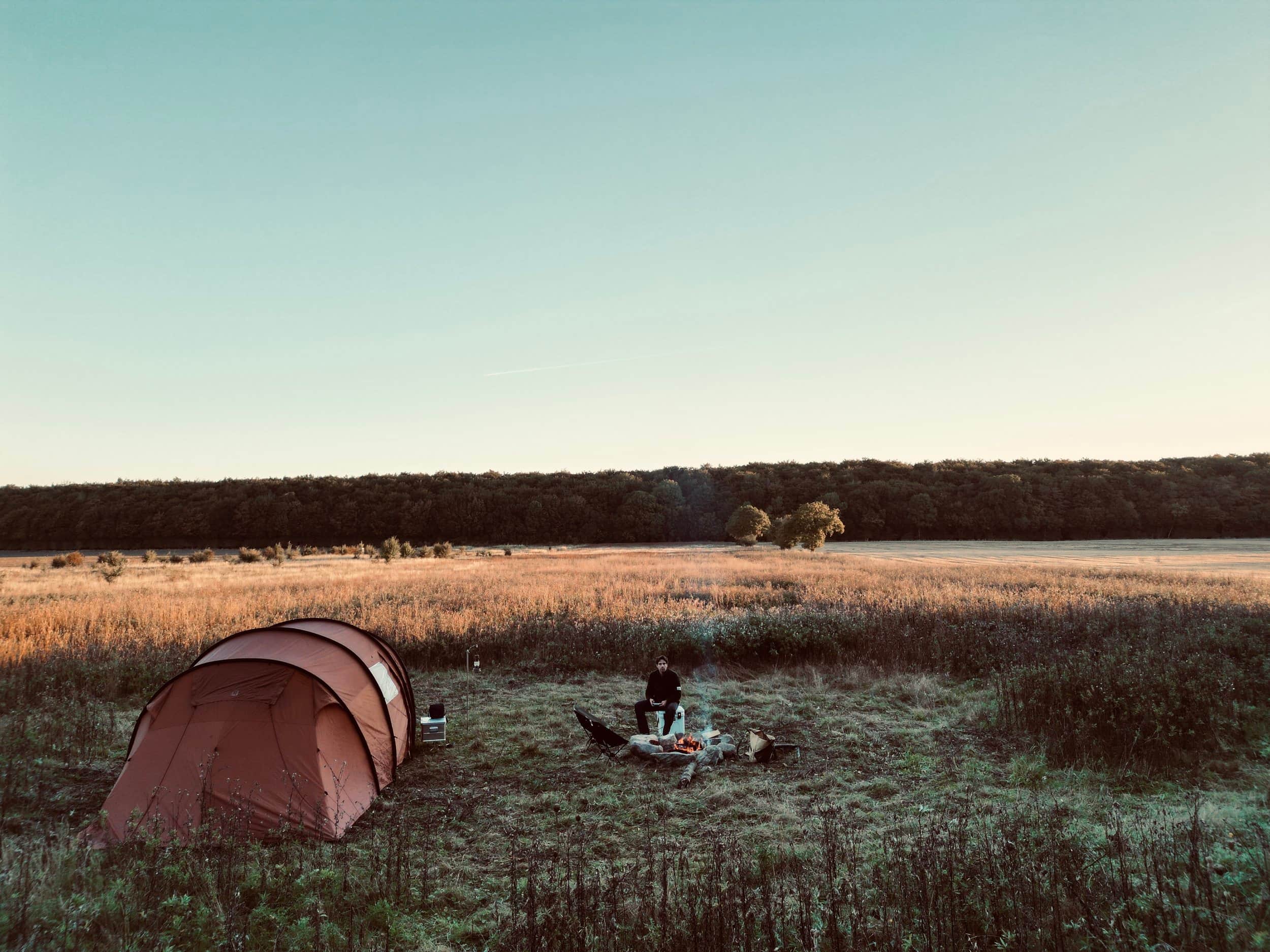 Rode tent en een persoon op een open veld bij een bosrand.