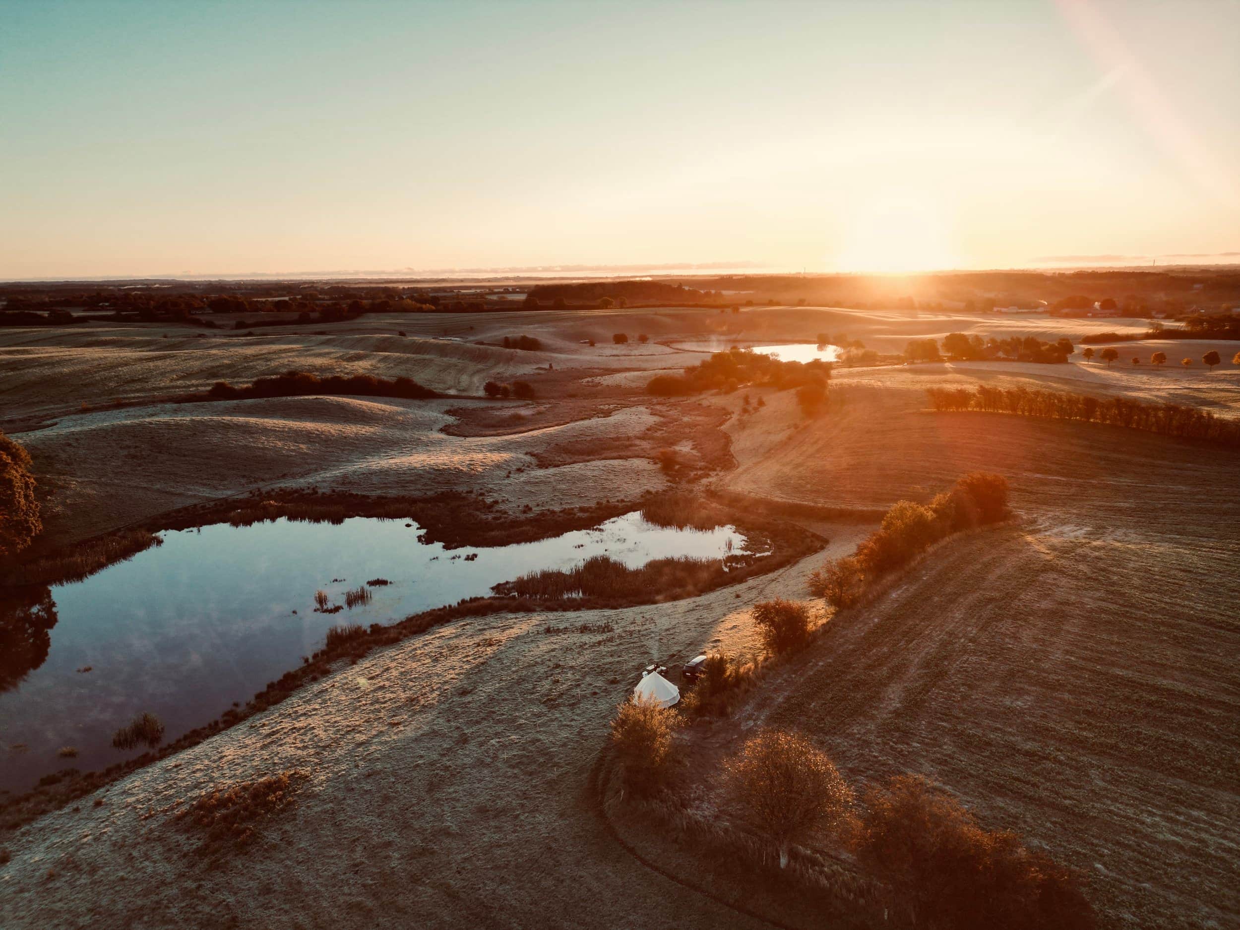 Luchtfoto van een meer en een tent in het landschap bij zonsondergang.