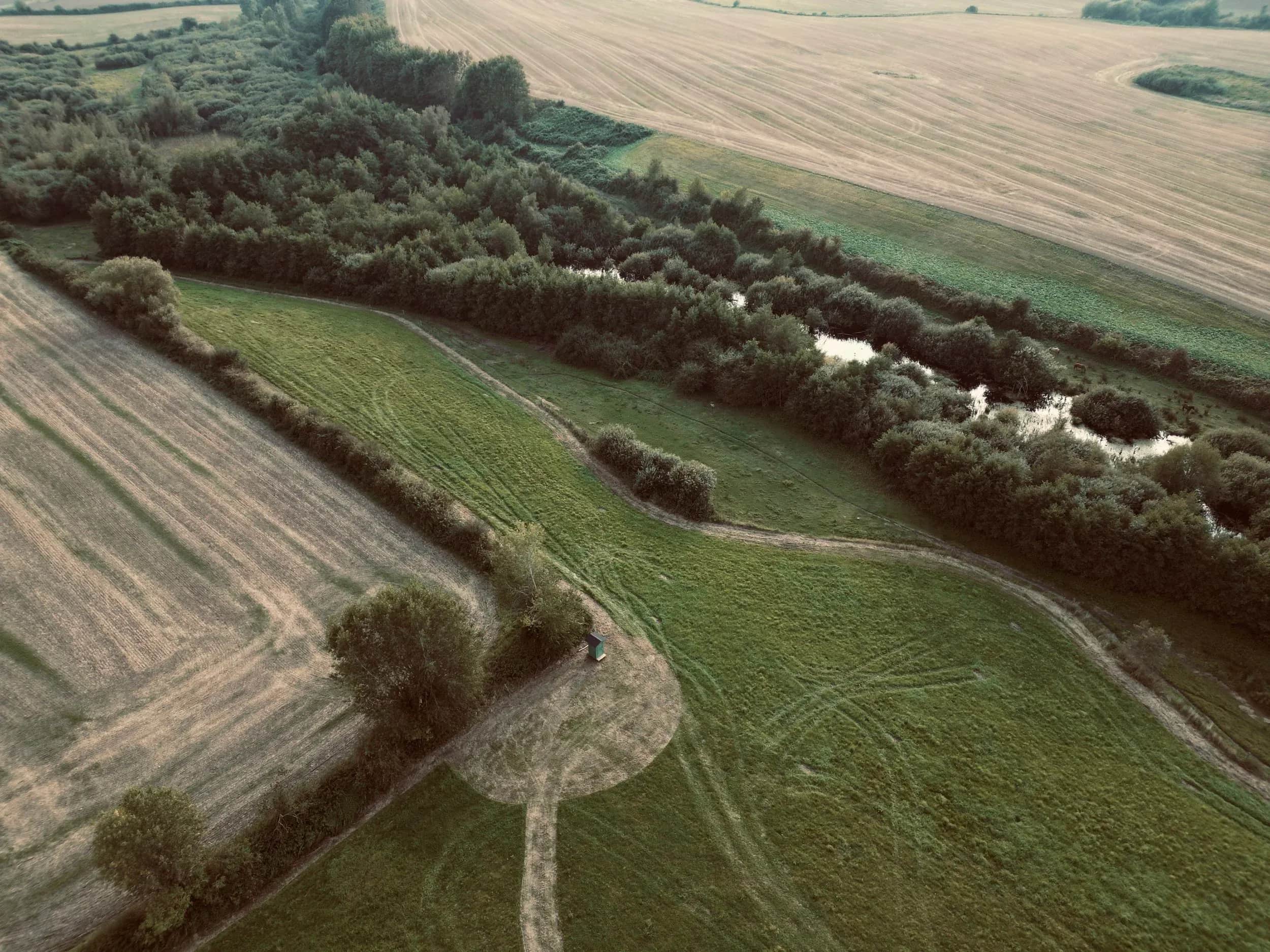 Luchtfoto van velden, heggen en een waterloop.