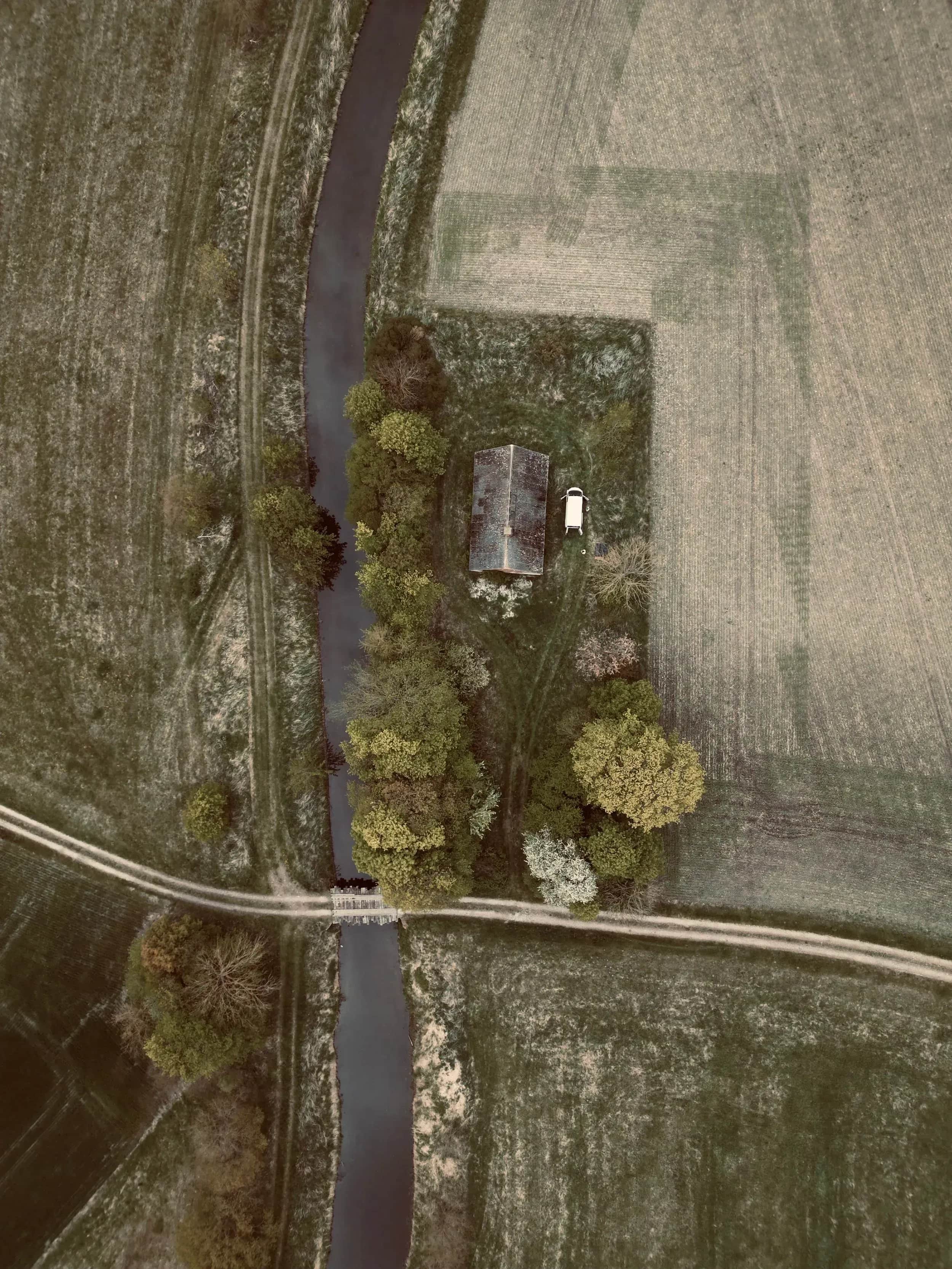 Luchtfoto van een beek, een weg en een klein huis tussen velden.