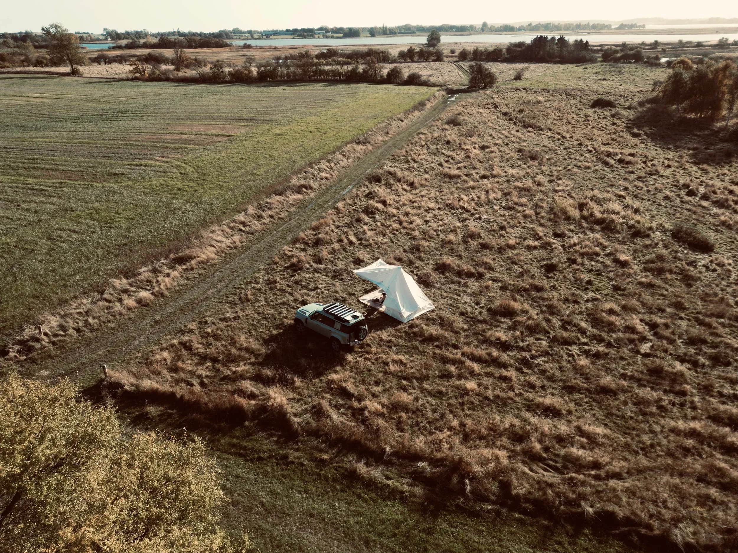 Aerial photo of a car and a tent in a field by a track.