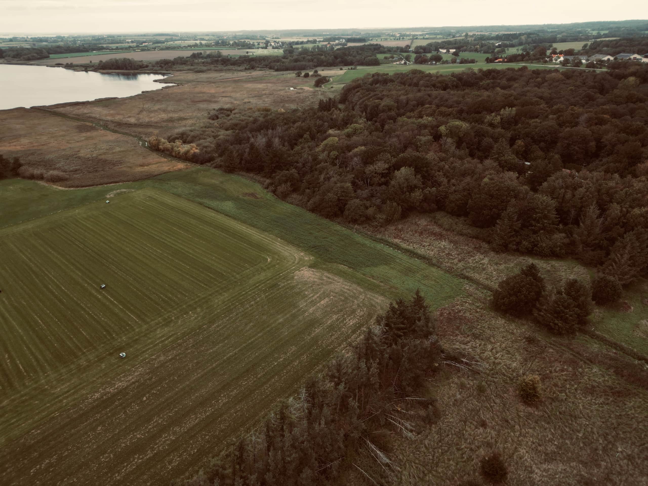 Flyfoto av Sandager Plads og landskapet rundt med jorder, skog og vann.